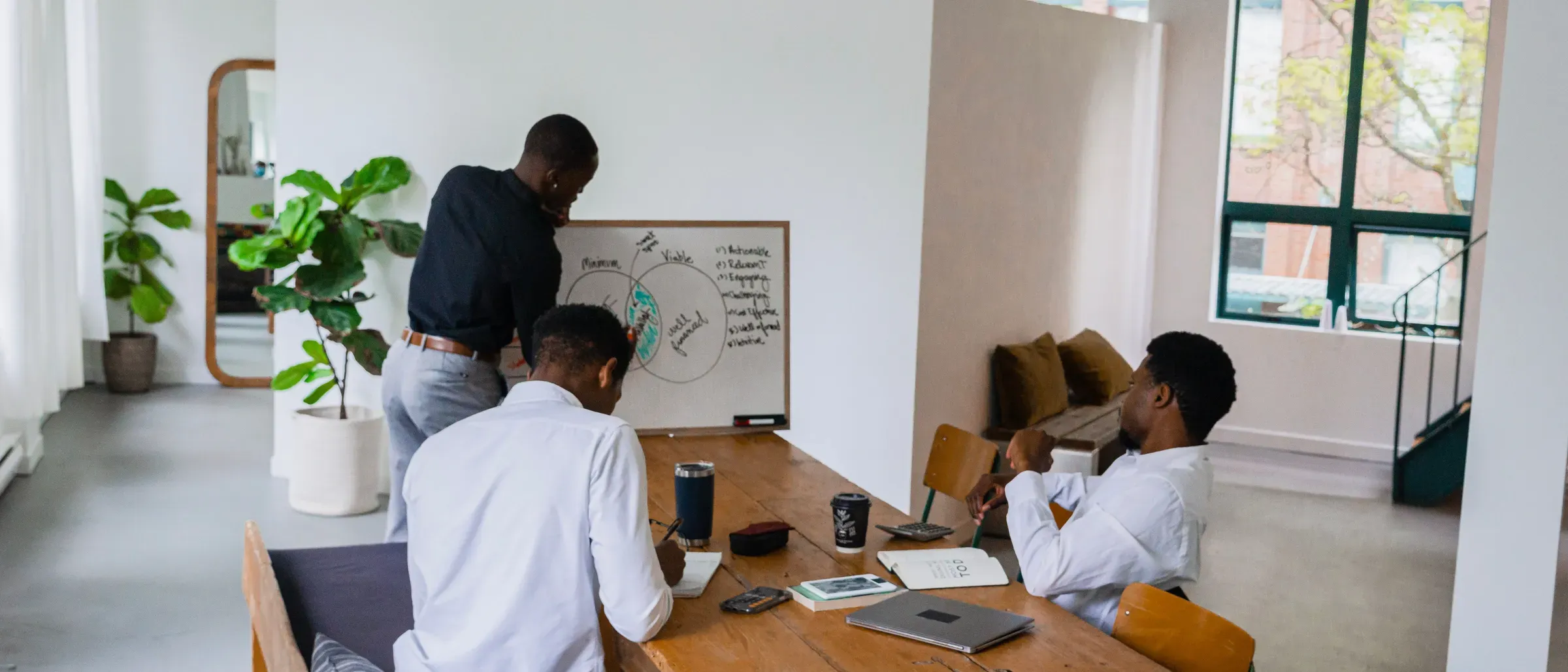 Drie collega's bespreken een schema op een whiteboard in een lichte kantoorruimte