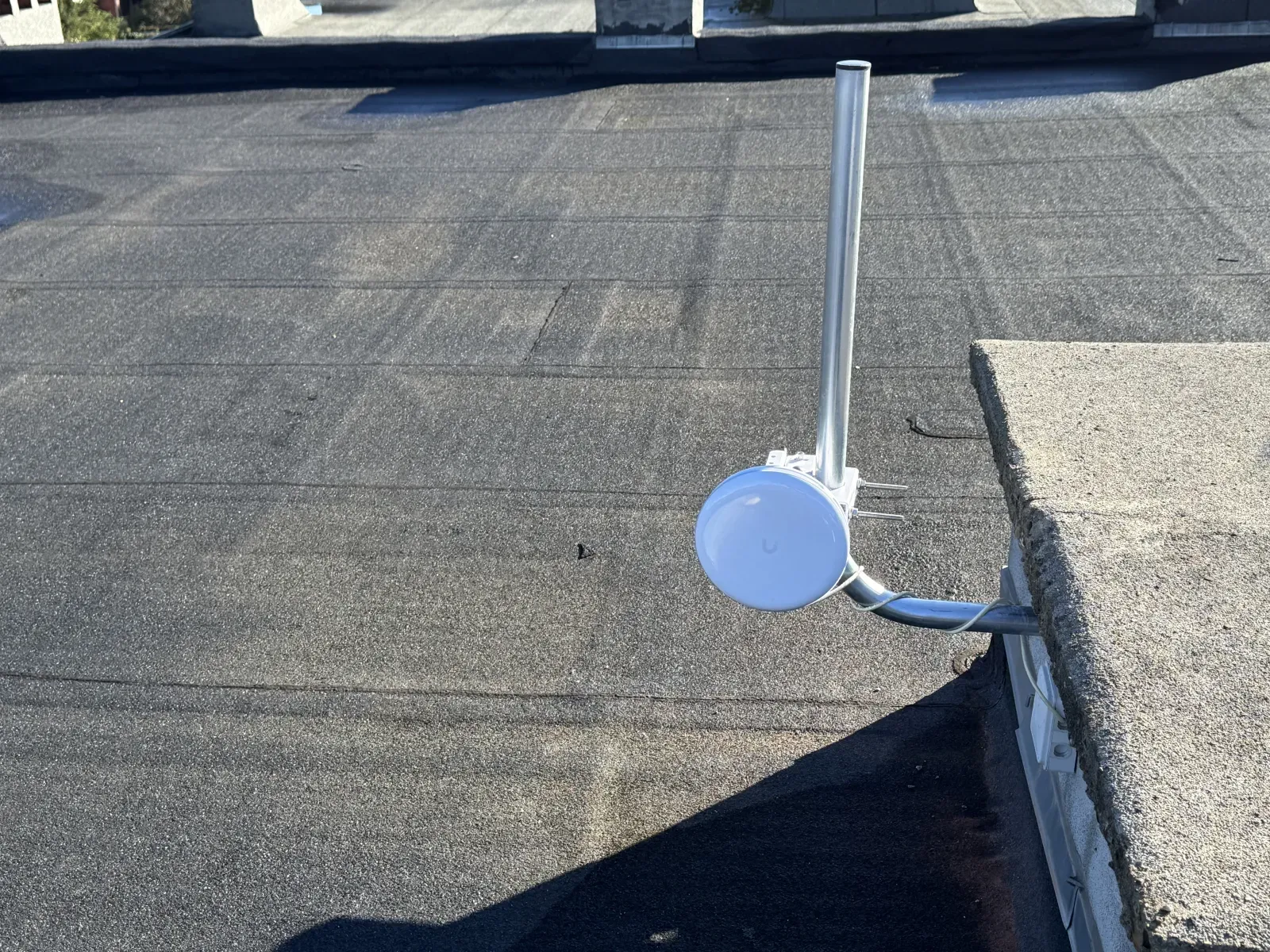 Ubiquiti antenna on a galvanised mast, fixed to the edge of the flat roof of a satellite site