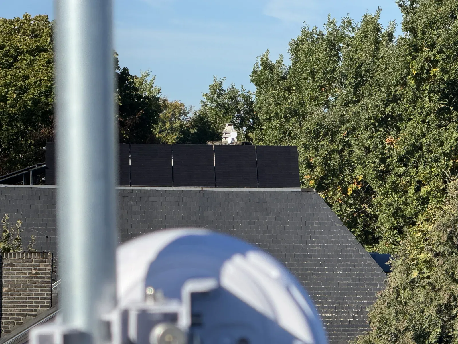 View from the roof of a satellite site towards the antennas beside the chimney of the main building, between the trees